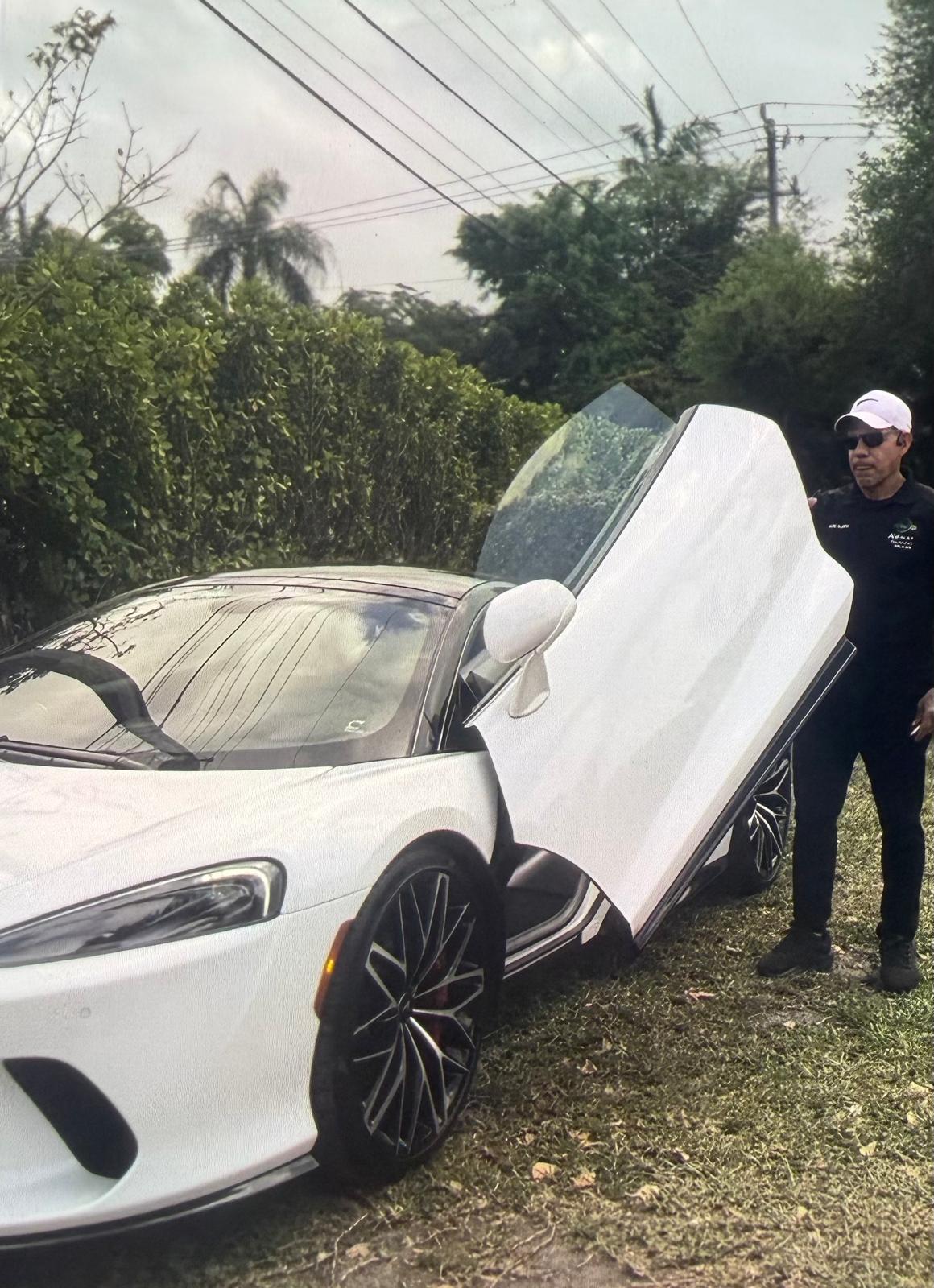 AV Valet attendant handling a white McLaren GT with dihedral doors open